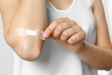 Female applying plaster on elbow against white background, closeup view