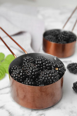 Fototapeta na wymiar Metal saucepans with ripe blackberries on marble table