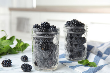 Fototapeta na wymiar Glass jars of tasty ripe blackberries on marble table