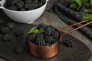 Fototapeta na wymiar Metal saucepan with tasty blackberries on grey table
