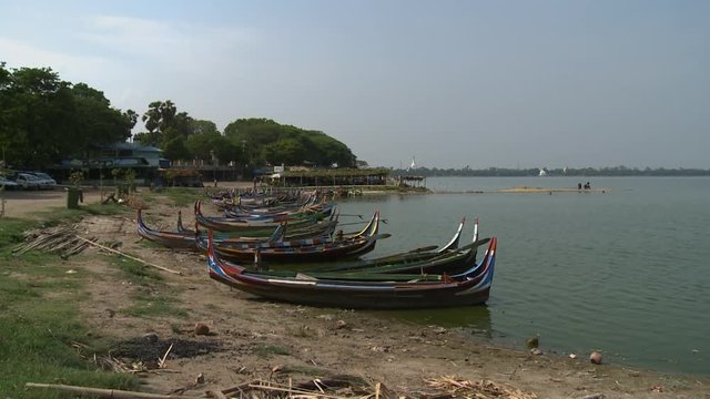 A wide shot of a person cleaning a boat painted in different colors in a row of many boats on the water