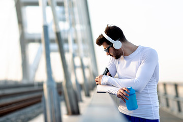 Man with heaphones resting before jogging and listen music with bottle of water on hand