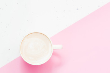 White cup of cappuccino with cinnamon on the light pink background, top view