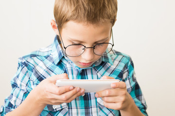 Handsome boy in glasses plays tablet. The concept of poor eyesight, harm of gadgets, myopia