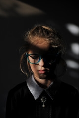 Fototapeta na wymiar mysterious little mindful girl with closed eyes wearing glasses and school uniform stands in darkness