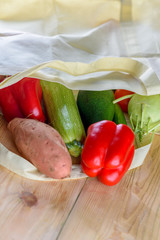 World free of plastic.Reusable eco friendly canvas grocery shopping bag with vegetables-sweet potato, zucchini, pepper, tomatoes, cucumber and avocado on wooden desk. Organic products. Less plastic.
