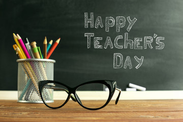 Glasses teacher and a stand with pencils on the table, on the background of a blackboard with...