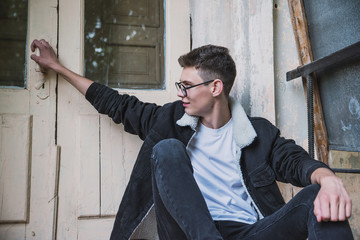 a young rebel in a jacket and jeans on the background of an old crumbling building with glasses and...