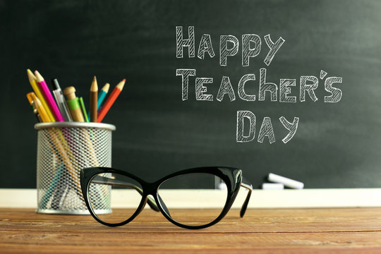 Glasses teacher and a stand with pencils on the table, on the background of a blackboard with chalk. The concept of the teacher's day. Copy space.