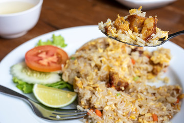 Spoon scooping fried rice with pork and vegetable on dish, Thai cuisine.