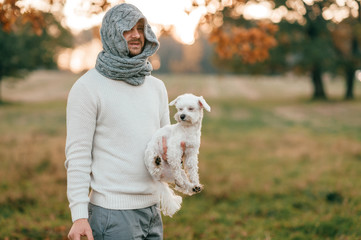 Strange man with wrapped face holding beautiful puppy in his hand outdoor at sunset.