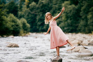 Young graceful ballerina girl balancing on stone in the river.