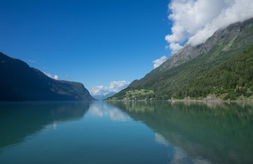 Fototapeta na wymiar Panoramic view of The Sognefjord (Sognefjorden), nicknamed the King of the Fjords. Te largest and deepest fjord in Norway. Symmetry created by reflections in the still ocean water. Bright midsummer.