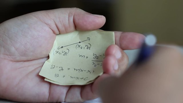 Student using formula math sheet to cheat on test. Hand of university student holding pencil doing math question in examination and cheating in test with answer piece of paper in hand. 