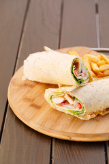 Wrapped sandwich chicken tortilla with fried potatoes and dipping sauce on wooden plate , wood background.