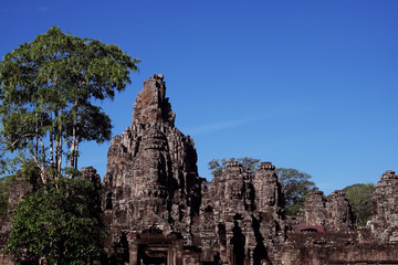 Fototapeta na wymiar The majestic towers of Bayon Temple, in Cambodia. Tall tropical trees. Beautiful landscape.