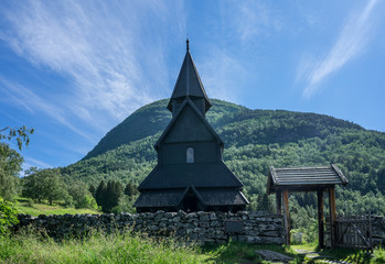 Fototapeta na wymiar Urnes Stave Church, a 12th-century stave building at Ornes, along the Lustrafjorden in bright midsummer day. Built with a rectangular nave and a narrower choir. World Heritage Site by UNESCO. Norway.