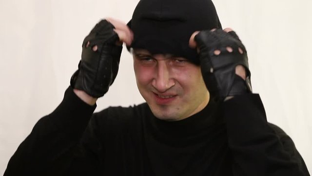 young cheeky caucasian man bandit with a smirk puts on a balaclava at the end of the video goes down, close-up