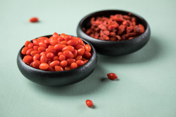 Frische und getrocknete Goji-Beeren Superfood in schwarzer Porzellan Schale auf Mint Grün Pastell Hintergrund