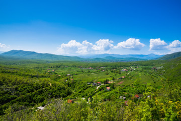 Fototapeta na wymiar Montenegro, Houses of vidrovan village in green valley surrounded by mountains and forest in country scenery of nature landscape with blue sky in springtime