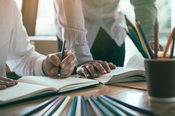 Two student reading textbook for test together in library.