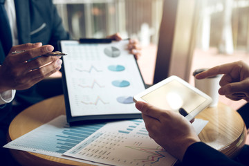 Managers are using tablets to analyze sales cost reports and explain summary reports to employees calculate and record summary information data in the office.