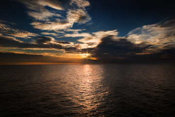 Ocean with sun setting through the clouds