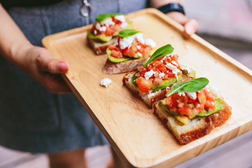 Avocado Toast with Cherry Tomatoes and Feta Cheese, Topping with Rocket leaves. Served on wooden plate.