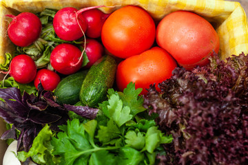 cucumbers, tomatoes, radishes, lettuce, basil, parsley in a box with a yellow napkin.