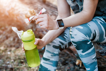 woman drinks amino acids and has a protein bar in the forest