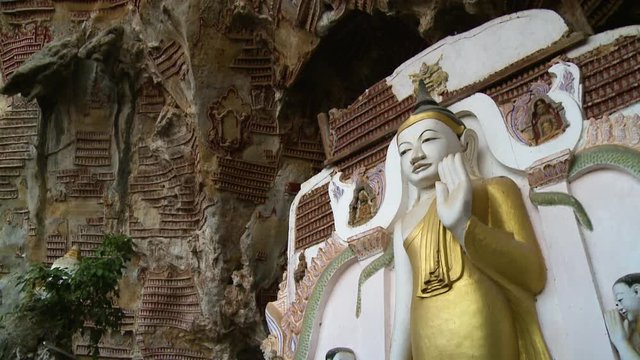Steady, straight on, medium wide shot of a Buddha statue and artifacts on a cave wall.