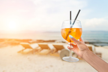 Woman holding Delicious classic iced aperol spritz cocktail with ice cubes on a hot tropical beach in summer sunshine