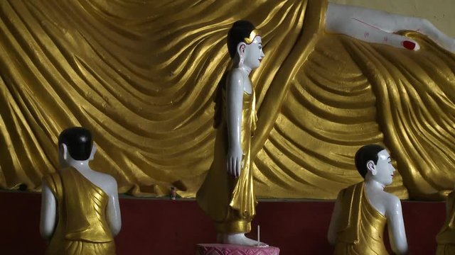 Steady, interior, medium close up of Buddha statue and miniature of sculptures.