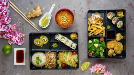 Japanese cuisine. lunch box set, sushi roll, salad, miso, chicken, sauce and wasabi on grey background.