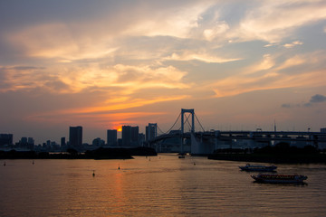 Silhouette of Rainbow Bridge and buildings in Odaiba Tokyo Bayduring sunset moment with 2 tourist boats in scene 