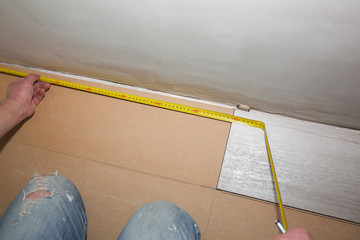 Worker making laminate flooring in apartment. Measure tape and pencil in hands. Maintenance repair renovation. Wooden parquet planks indoors.