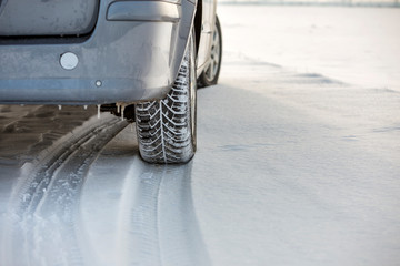 Close up of a car tire parked on snowy road on winter day. Transportation and safety concept.