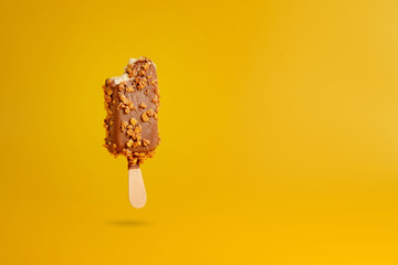 chocolate ice cream popsicle on yellow background bitten off a piece hanging in the air