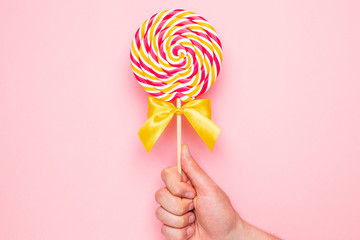 Colorful lolipop with pink, yellow and white spiral in hand on pink background