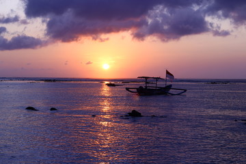 Naklejka na ściany i meble Last rays of tropical sun with fishing boat in Kuta, Bali, Indonesia