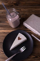 A piece of cheesecake with a chocolate heart on it, a glass mug of coffee and a notebook on a wooden background. Coffee break. Vertical 
