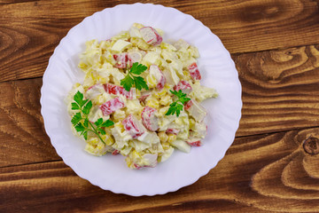 Salad with crab sticks, sweet corn, chinese cabbage, eggs and mayonnaise on wooden table