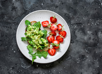 Healthy snack, breakfast - sandwich with avocado and fresh strawberries on a dark background, top view