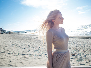 Young cheerful girl on the seashore. Young blonde woman smiling. Trendy beige skirt