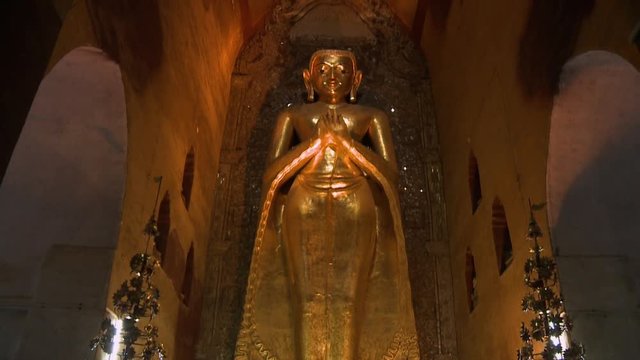 A low angle shot of a tall statue of buddha standing with hands clasped inside a Ananda temple in Burma