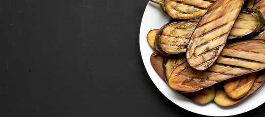 Grilled eggplant on a white plate on a black surface. Space for text.