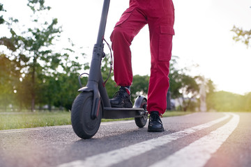 Obraz premium Close up of teen riding electric kick scooter in the park at sunset 