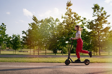 Cute teenager girl riding electric kick scooter in the park at sunset          © D'Action Images