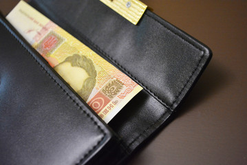 A black women's purse with money made from genuine cowhide leather and gold accessories is located on a matte brown background.