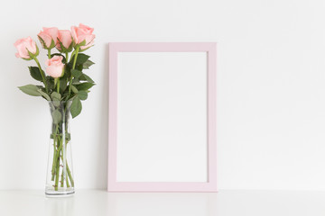 Pink frame mockup with a bouquet of pink roses in a glass vase on a white table. Portrait orientation.